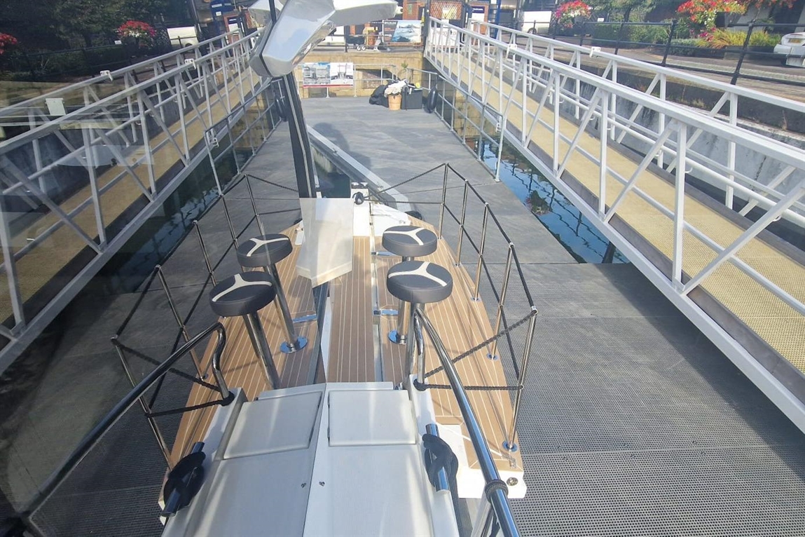 View from above of a boat dock showing a wooden deck, black stools, and a modern walkway leading to a nearby dock.
